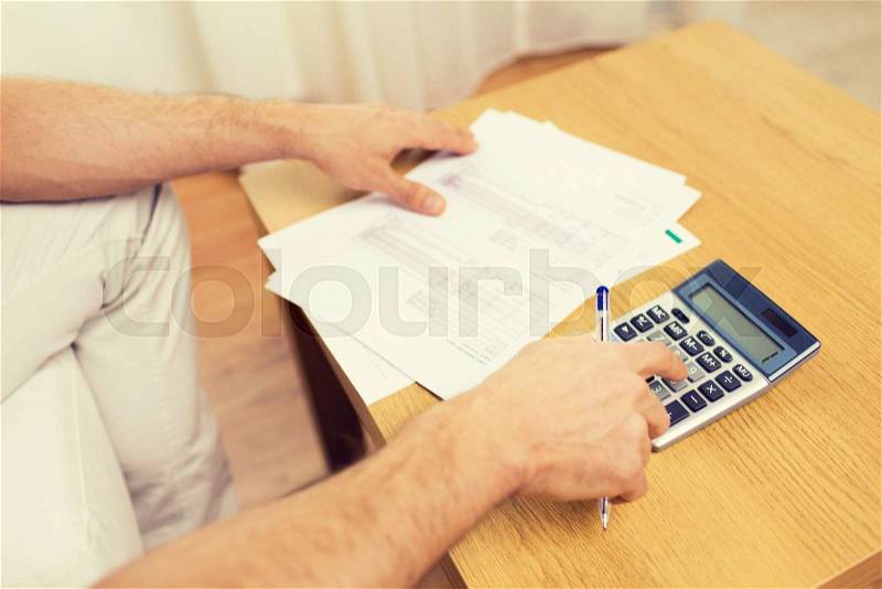 Business, savings, finances and people concept - close up of man hands with papers and calculator at home, stock photo