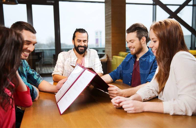 Leisure, people and holidays concept - smiling friends discussing menu at restaurant, stock photo