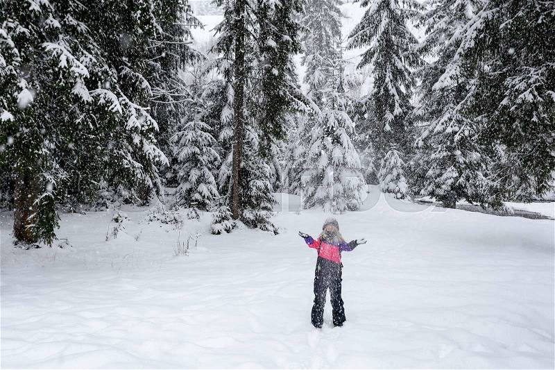 Happy girl in pink ski suit throwing snow in the air in winter holidays in the winter snow-covered forest. Snowing, stock photo