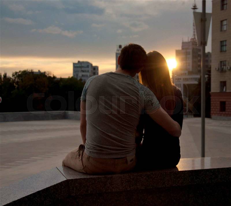 Happy romantic couple sitting in street of city and enjoying sunset, stock photo