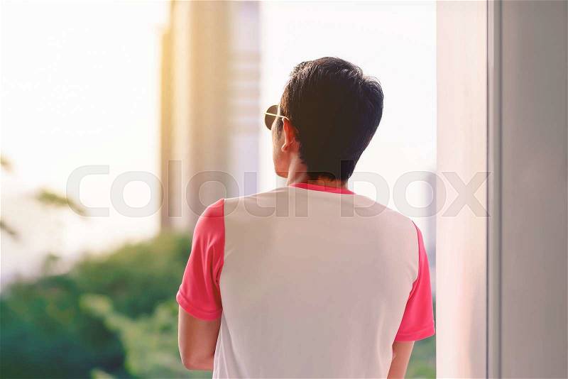 Man in pink and white t-shirt looking outside at sunset, stock photo