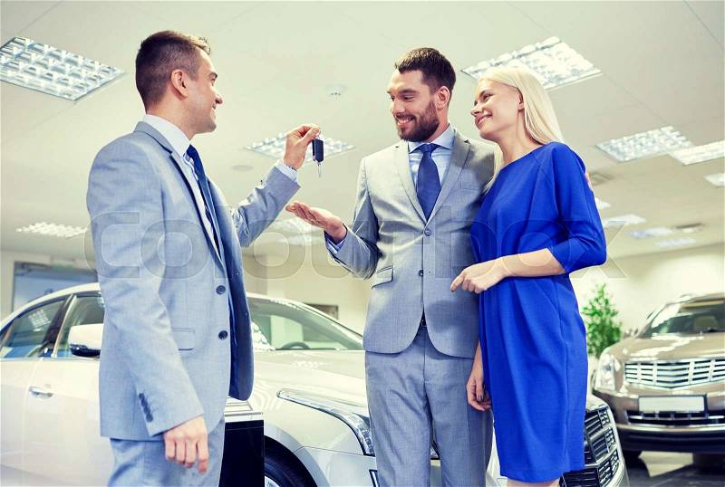 Auto business, sale and people concept - happy couple with dealer giving car key in auto show or salon