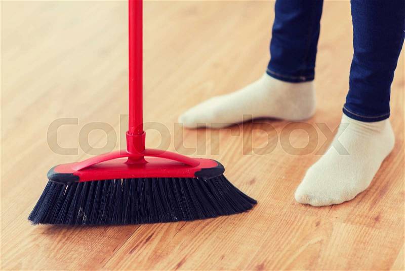 People, housework, cleaning and housekeeping concept - close up of woman legs with broom sweeping floor at home, stock photo