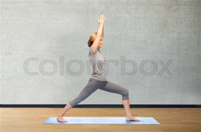 Fitness, sport, people and healthy lifestyle concept - woman making yoga warrior pose on mat over gym room background, stock photo