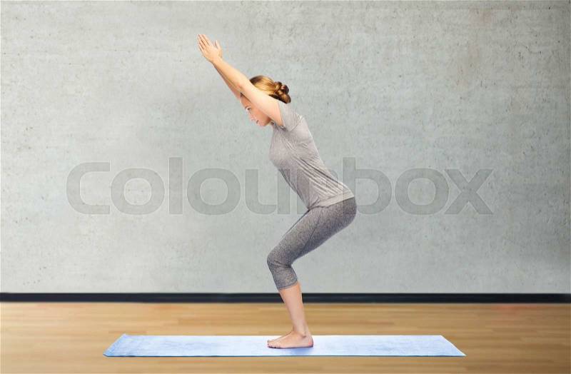 Fitness, sport, people and healthy lifestyle concept - woman making yoga in chair pose on mat over gym room background, stock photo