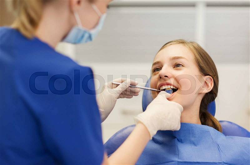 People, medicine, stomatology and health care concept - happy female dentist with mirror checking patient girl teeth up at dental clinic office, stock photo