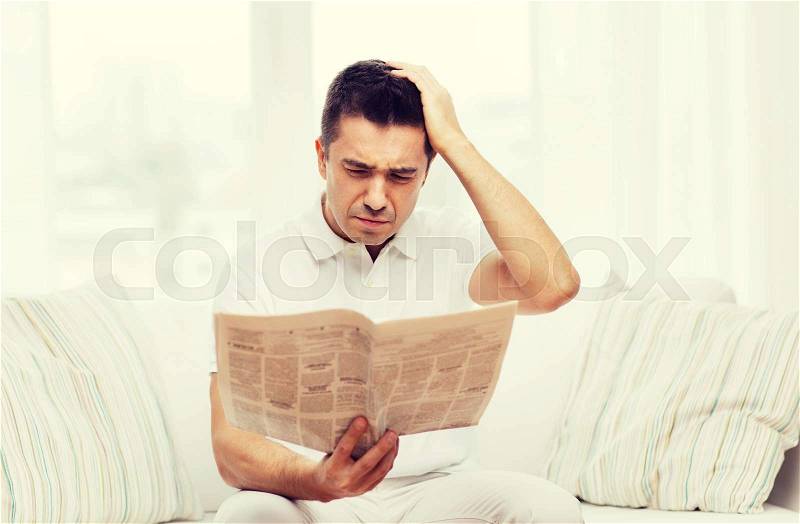 Leisure, information, people and mass media concept - sad man reading newspaper at home, stock photo