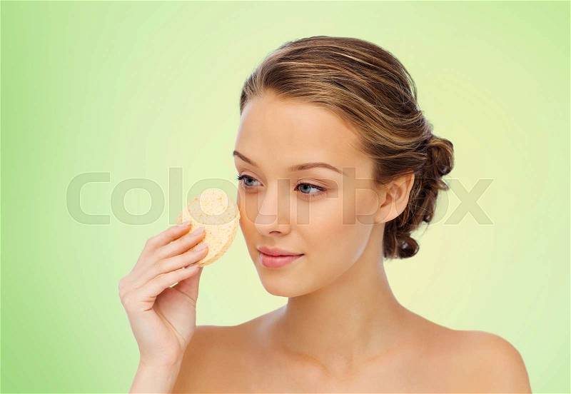 Beauty, people and skincare concept - young woman cleaning face with exfoliating sponge over green natural background, stock photo