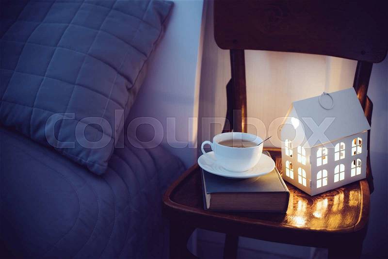 Cozy evening bedroom interior, cup of tea and a night light on the bedside table. Home interior decor with warm light, stock photo