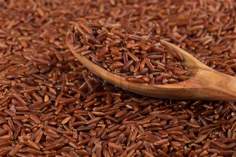 Red rice in a wooden spoon on red rice background, stock photo