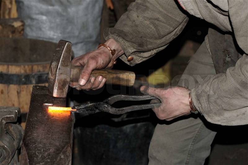 Blacksmith working metal with hammer on the anvil in the forge, stock photo