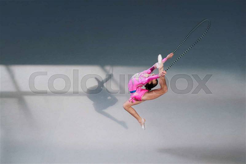 Side view of female gymnast in pink dress with jumping rope. Silhouette shadow on floor, stock photo