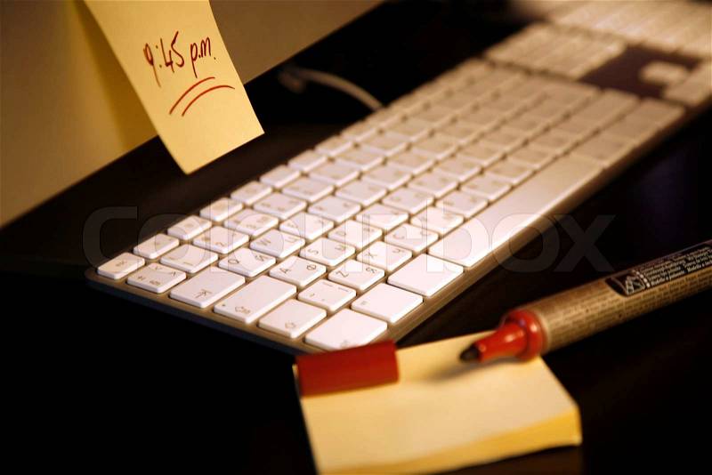 Post-it note with a reminder sticked on a computer screen with keyboard and a marker, stock photo