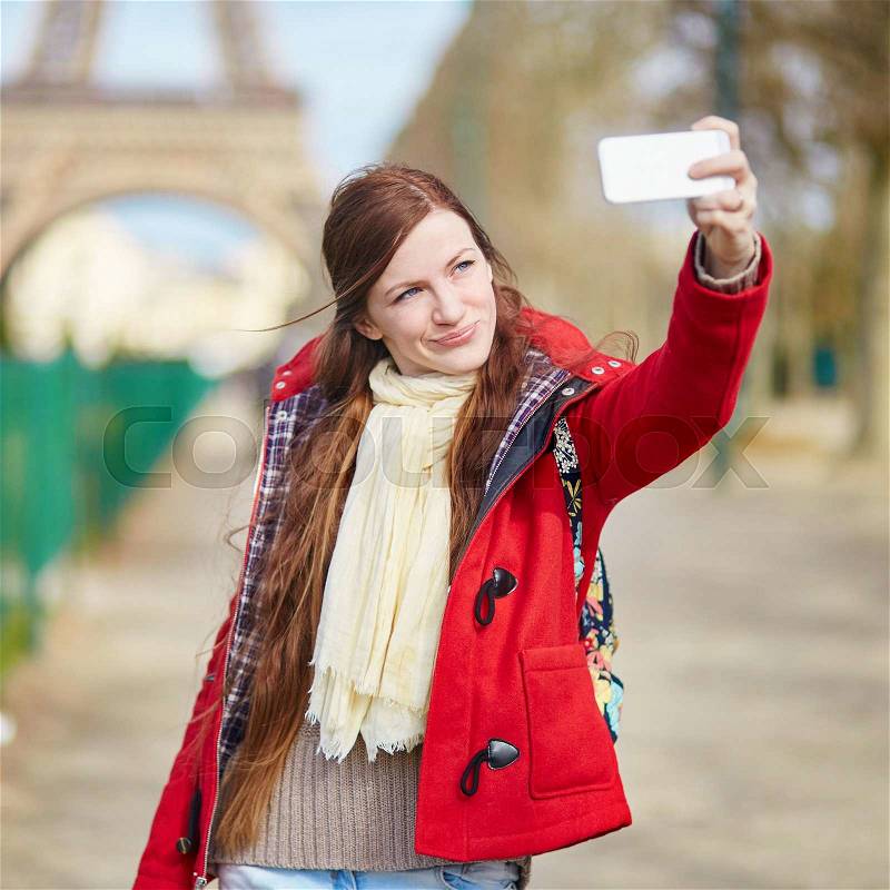 Beautiful young tourist in Paris taking selfie using her mobile phone near the Eiffel tower, stock photo