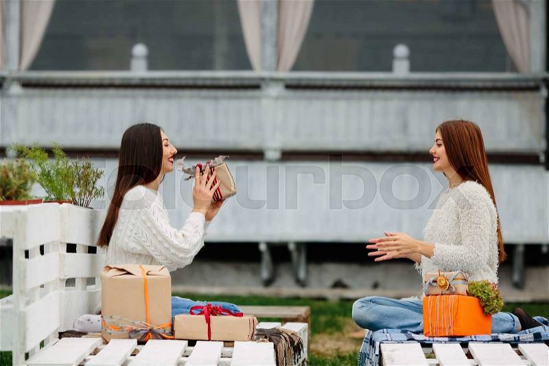 Two beautiful girls sitting on a bench and throws gifts to each other, stock photo