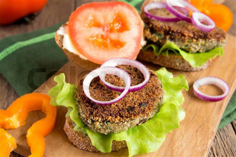 Vegetarian lentil burger with vegetables on wooden cutting board, stock photo