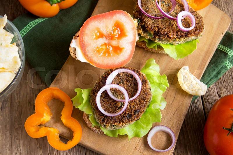 Vegetarian lentil burger with vegetables on wooden cutting board, stock photo