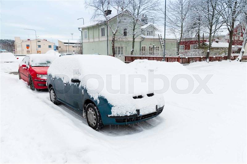 Cars covered with snow parked along snowy street in Finland, stock photo
