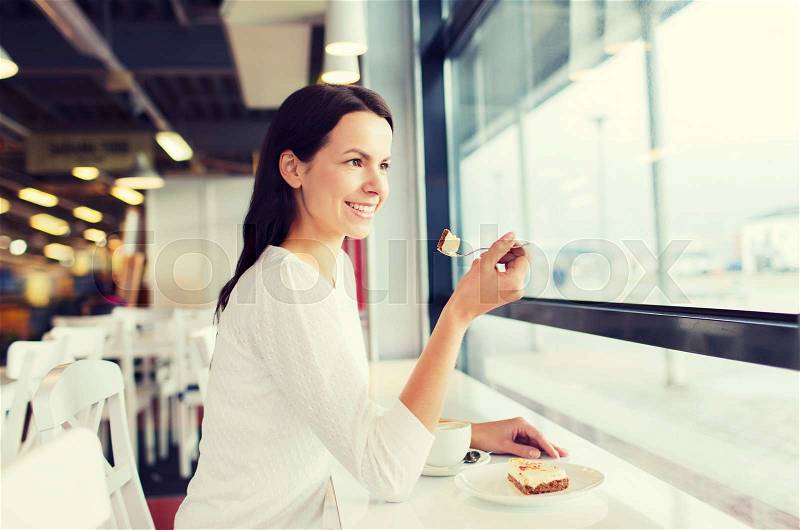 Leisure, drinks, people and lifestyle concept - smiling young woman eating cake and drinking coffee at cafe, stock photo