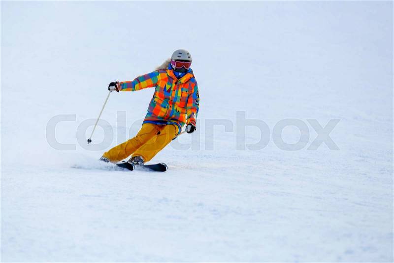 Male skier skiing in fresh snow on ski slope on a sunny winter day at the ski resort. Skier in red ski suit and mask slides fast while skiing from slope, stock photo