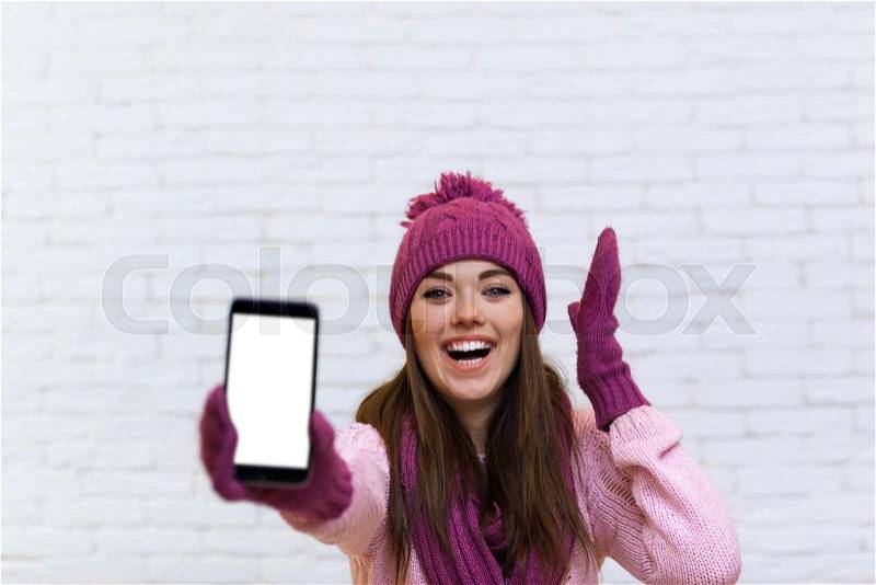 Portrait Of Attractive Teenage Girl Displaying Cell Smart Phone Touch Screen Empty Space Over White Brick Background, stock photo
