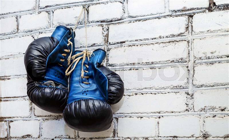 A pair of old blue and black boxing gloves hanging on white brick wall background, stock photo