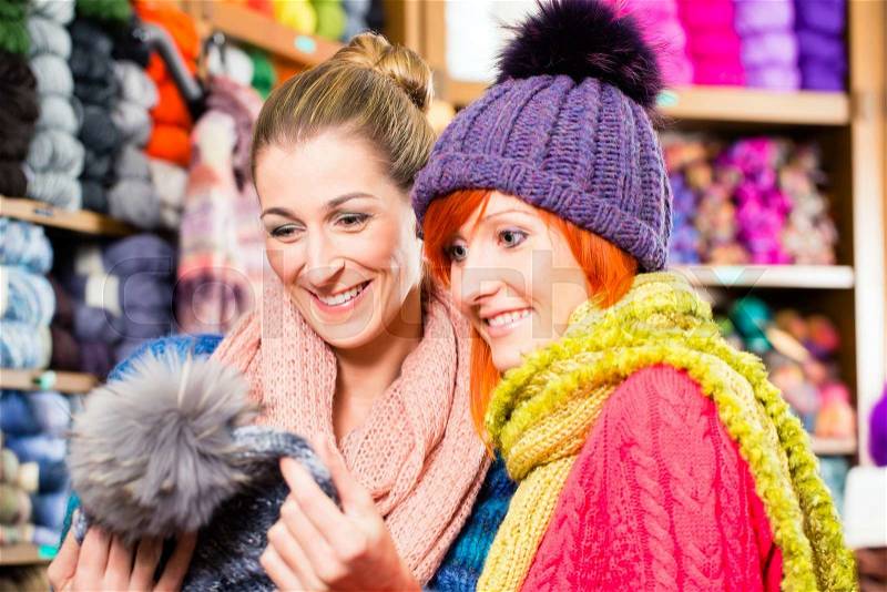 Young women buying colorful bobble hat in knitting fashion textile store, stock photo