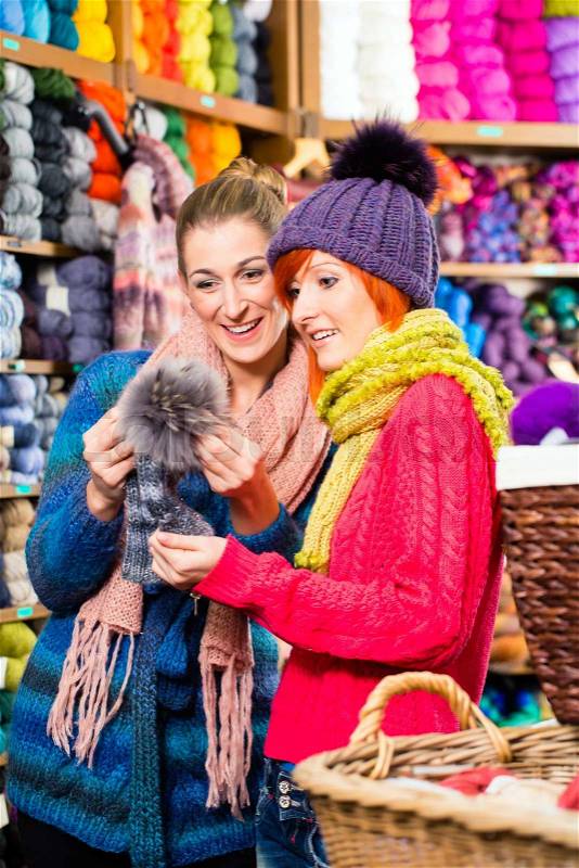 Young women buying colorful bobble hat in knitting fashion textile store, stock photo