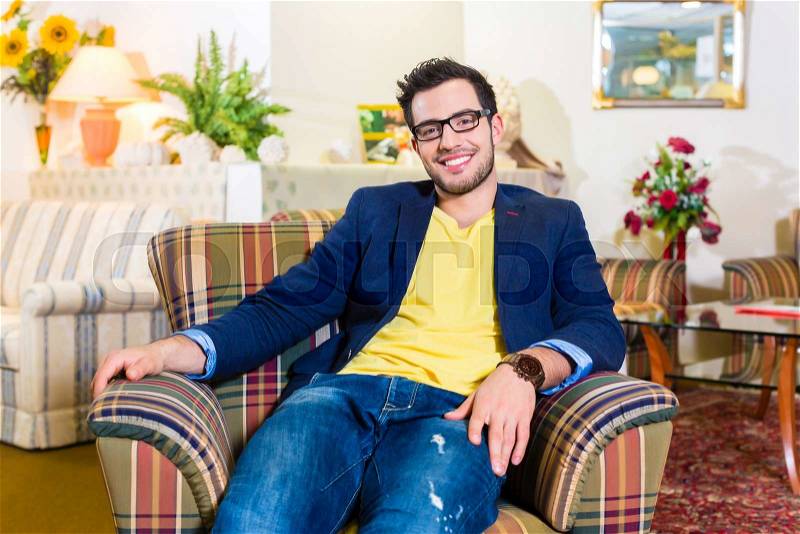 Young man testing and buying armchair in furniture store, stock photo