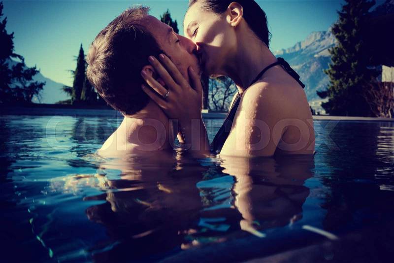 Woman and mean in honeymoon kissing in pool, filtered image, stock photo