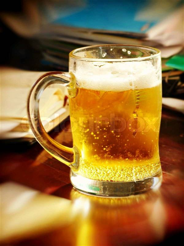 Lunch break-time.Beer glass on table with notebooks.Soft bokeh.Toned image, stock photo