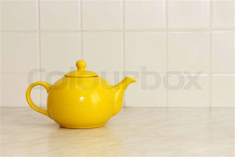 Yellow ceramic teapot on white kitchen table and ceramic tile background, stock photo