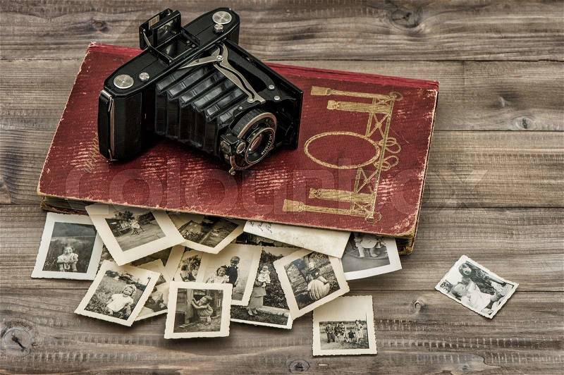 Antique film camera and photo album with old pictures on wooden table, stock photo