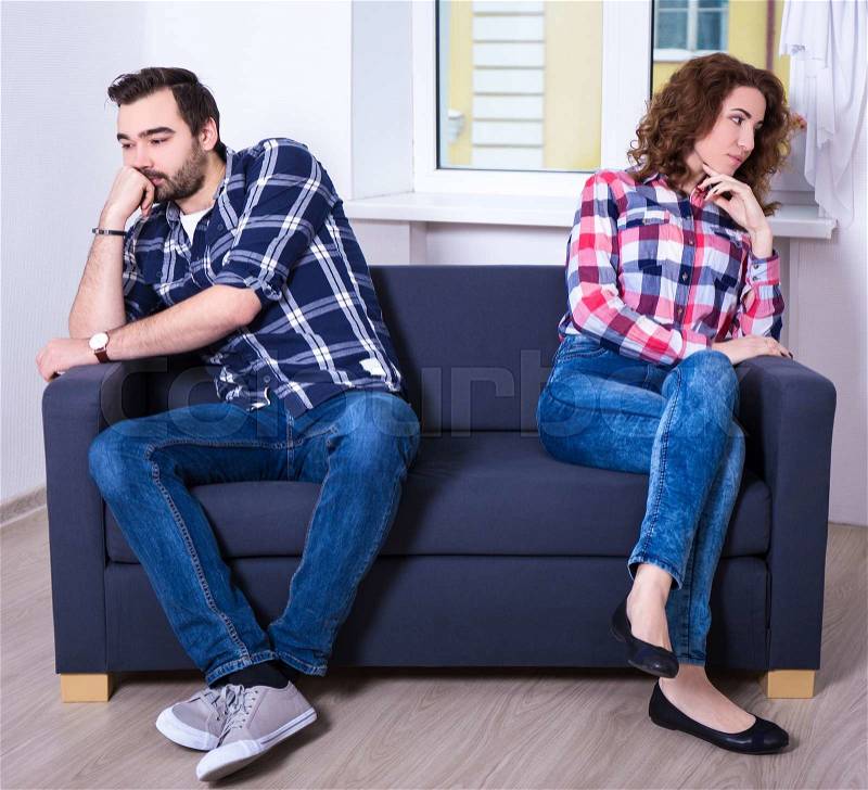 Portrait of displeased couple sitting back to back on sofa in living room, stock photo