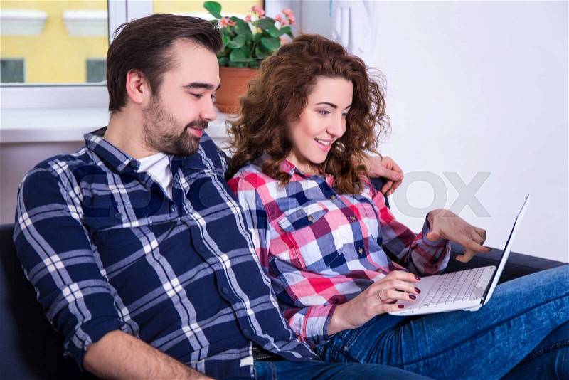 Online shopping concept - cheerful couple searching something in internet on laptop at home, stock photo