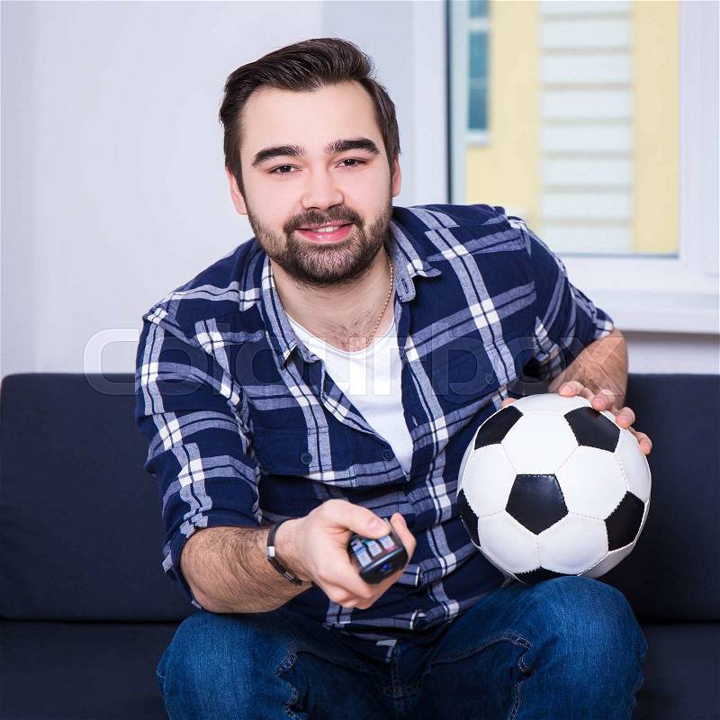 Happy young man watching soccer on tv, stock photo