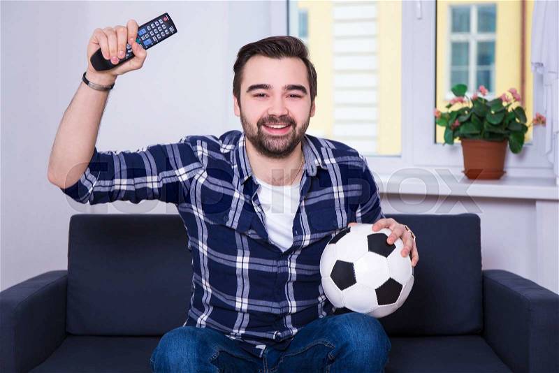 Happy young handsome man watching football on tv at home, stock photo