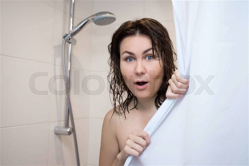 Young beautiful surprised woman covering her body with curtain in shower, stock photo