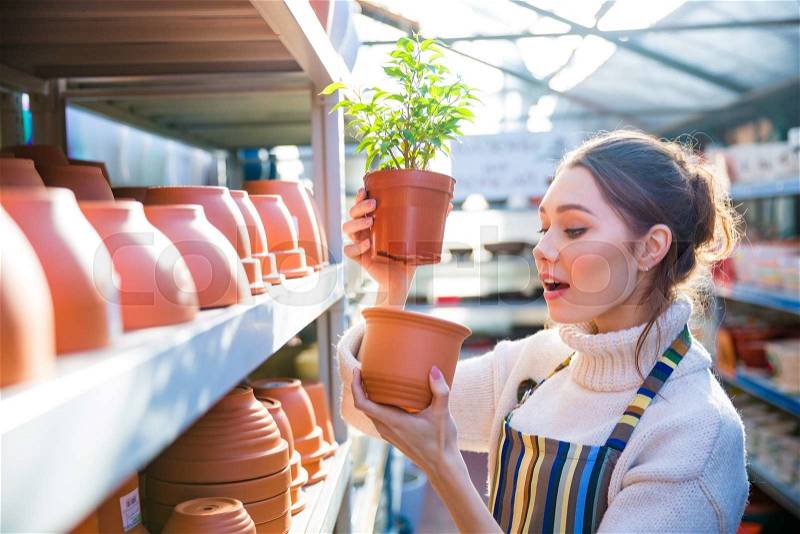 Pensive woman gardener choosing pot for plant in store, stock photo