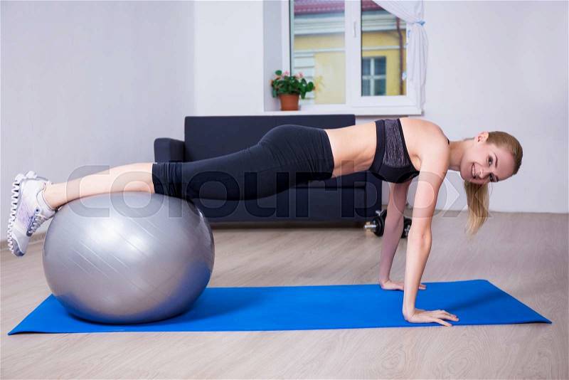 Beautiful woman doing push up exercise with fit ball at home, stock photo