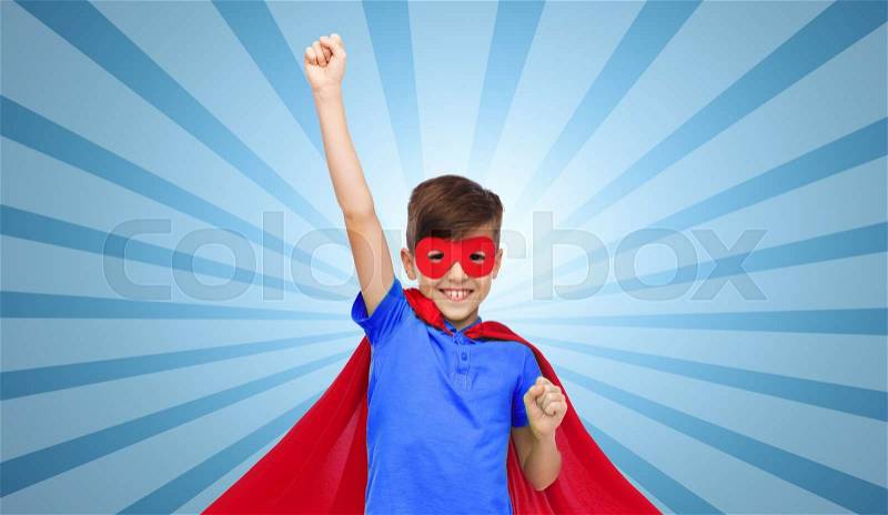 Carnival, childhood, power, gesture and people concept - happy boy in red super hero cape and mask showing fists over blue burst rays background, stock photo