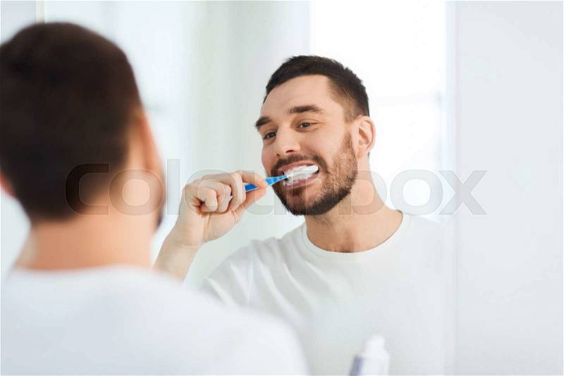 Health care, dental hygiene, people and beauty concept - smiling young man with toothbrush cleaning teeth and looking to mirror at home bathroom, stock photo