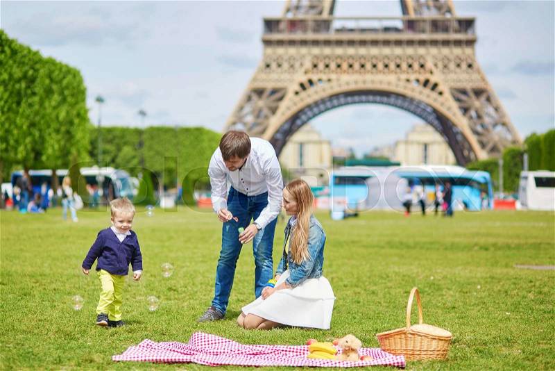 Happy family of three, mother, father and little toddler boy, having picnic in Paris near the Eiffel tower, stock photo