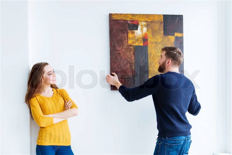 Young couple hanging picture on the wall at home, stock photo