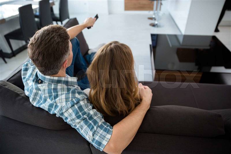 Back view of beautiful couple watching tv on sofa in living room , stock photo