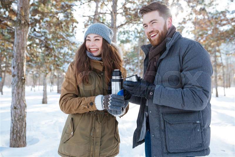 Laughing couple standing with thermos in winter park, stock photo