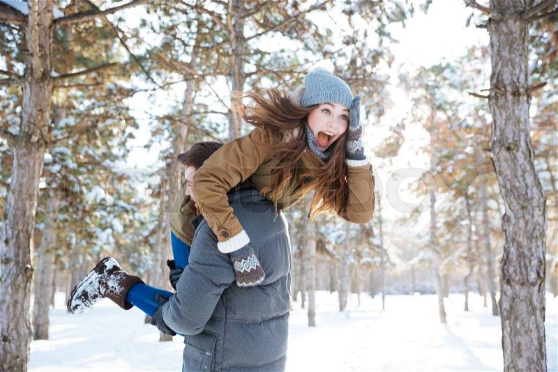 Man carrying cheerful woman on his shoulders in winter park, stock photo
