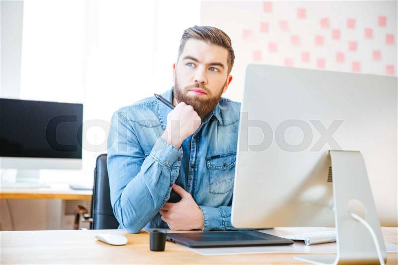 Pensive attractive modern designer sitting on workplace in office and thinking, stock photo