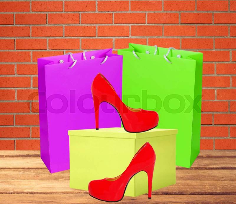 Red woman shoe, yellow gift box and shopping bags on wooden floor over brick wall, stock photo