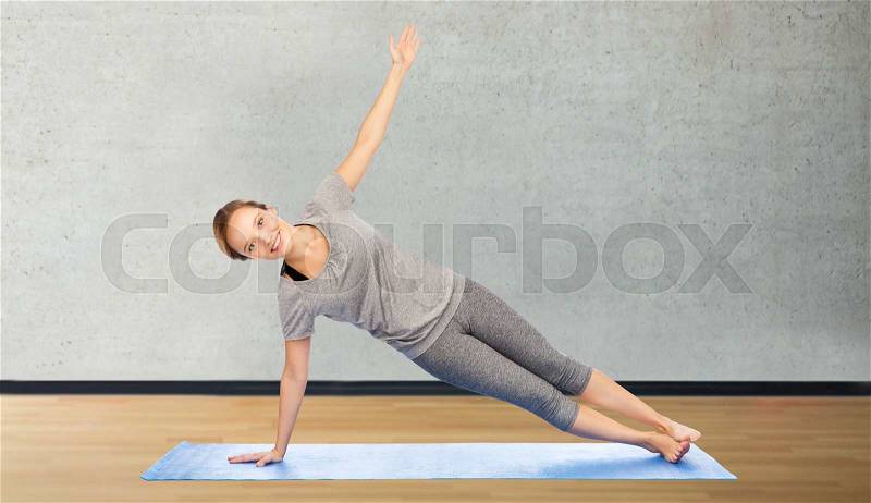 Fitness, sport, people and healthy lifestyle concept - woman making yoga in side plank pose on mat over room or gym background, stock photo